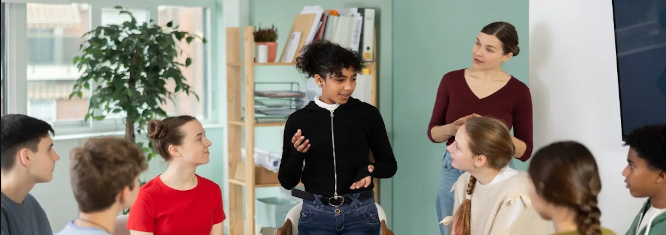 Teenage girl standing and speaking to a small seated group of peers